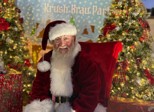 Santa Claus sitting on a red chair surrounded by Christmas decorations.