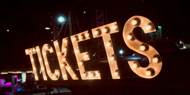Illuminated marquee letters spelling 'TICKETS' at night.