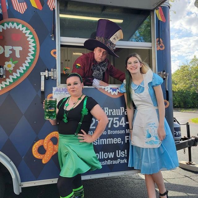 Three people in festive costumes posing by a decorated food truck.